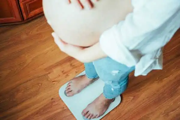 Image of woman weighing herself and experiencing weight gain through pregnancy Kirkby in Ashfield